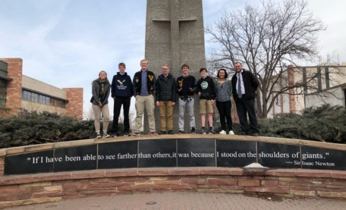 Students standing on top a quote stating "If I have been able to see farther than others, it was because I stood on the shoulders of giants." - Sir Isaac Newton