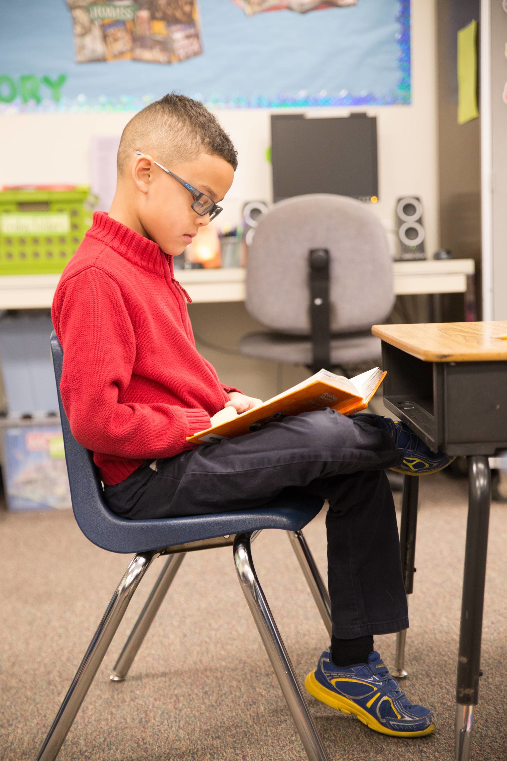 Young kid sits in a classroom reading a book