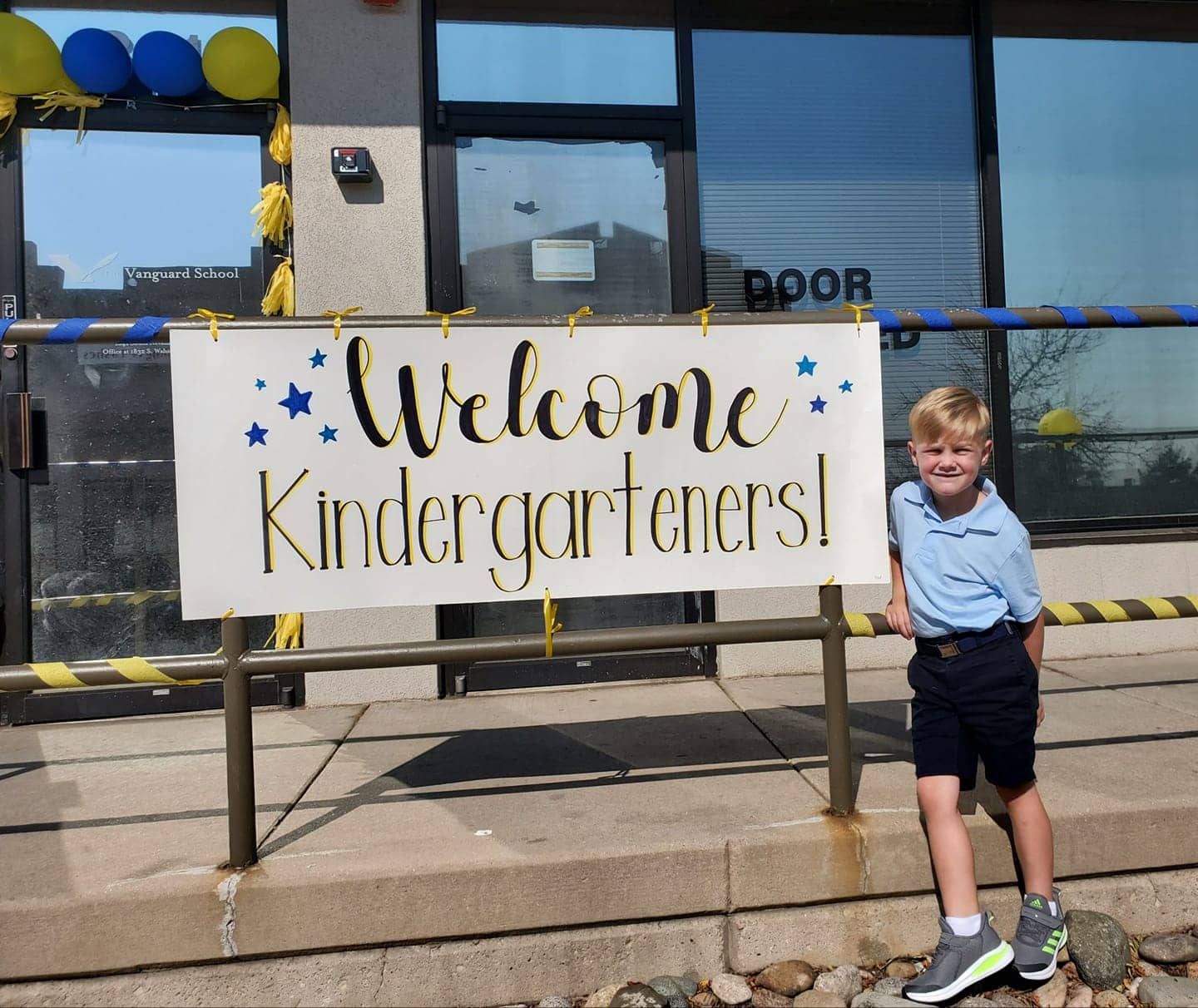 Kindergarten boy stands next to a welcome sign for back-to-school orientation