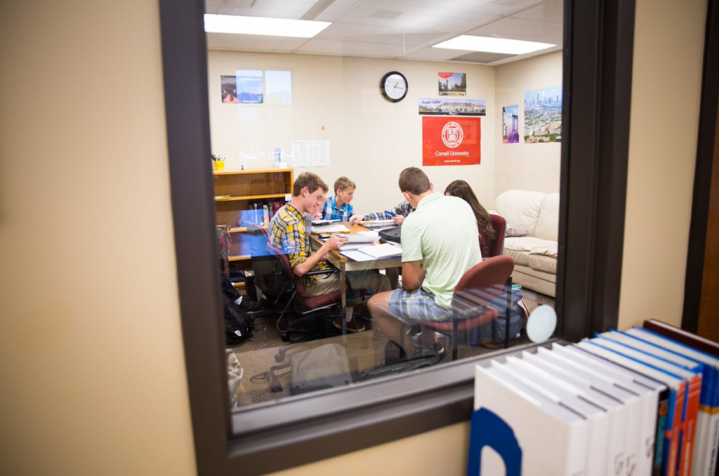 A view through a school classroom door showing a small group of students sitting around a table studying